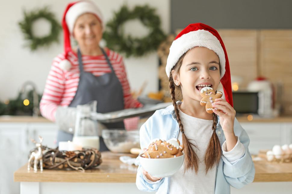 Free Image of Young girl with Santa hat eating gingerbread cookie happily 
