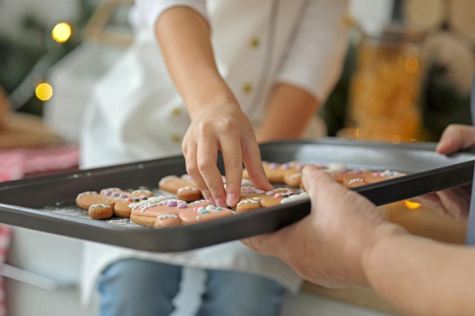 Free Image of Child reaching for cookie from baking tray held 