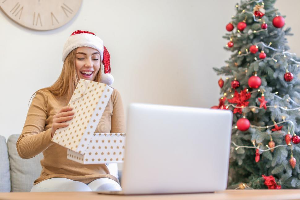 Free Image of Woman joyfully unwrapping a Christmas present online 