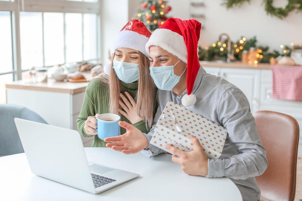 Free Image of Couple in Santa hats video chatting holding a gift box 
