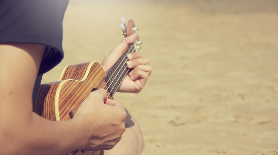 Free Image of Person playing a ukulele on the beach during the day. 