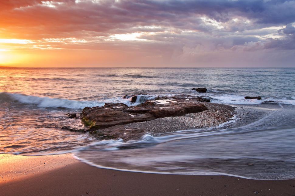 Free Image of Golden sunset over ocean waves with rocky foreground scene. 