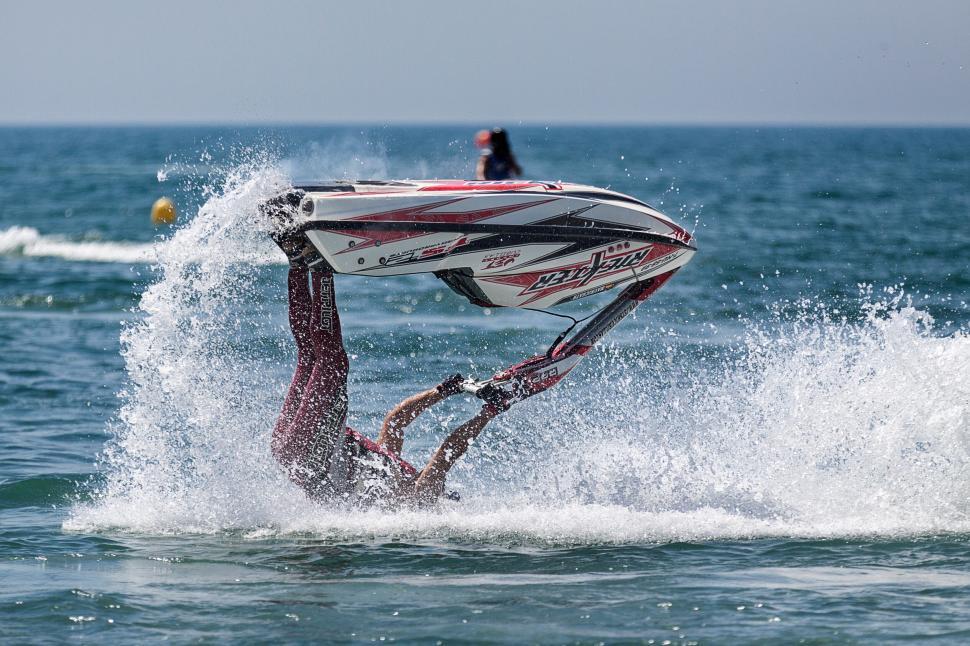 Free Image of Man flips on jet ski in midair with water splashing. 