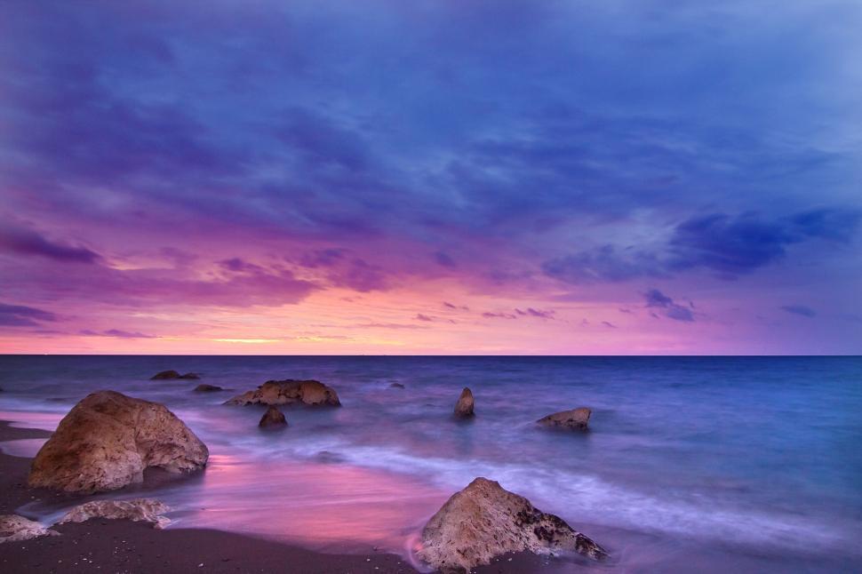 Free Image of Colorful sunset over rocks and sea with vibrant clouds. 