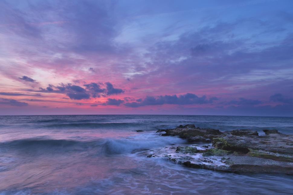 Free Image of Vibrant sunrise over the sea with rocks and waves. 