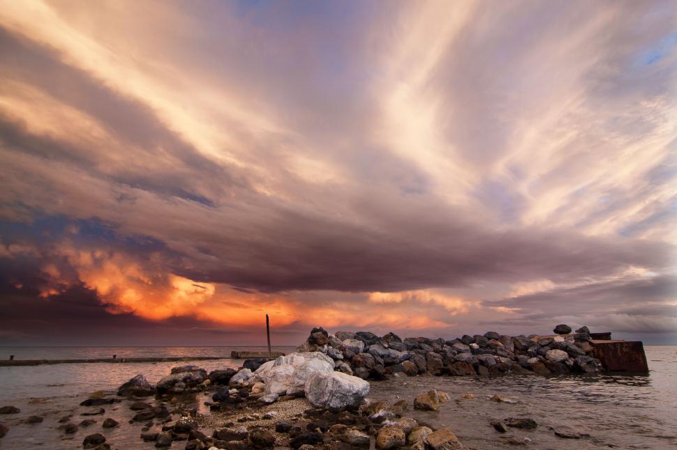 Free Image of Serene ocean sunset with rocks under dramatic clouds. 