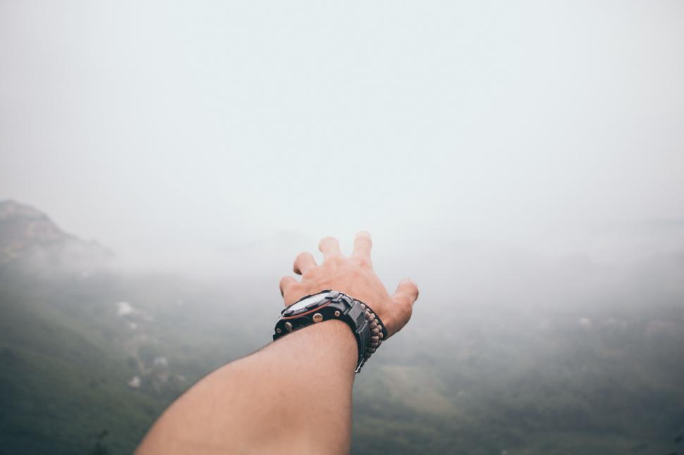 Free Image of Hand reaching out towards foggy mountains in the distance. 