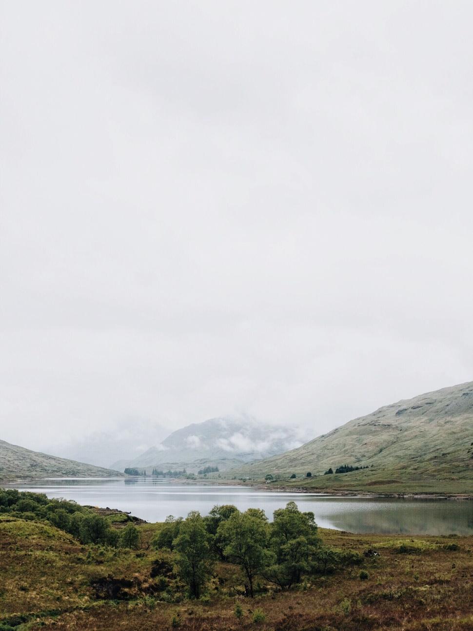 Free Image of Serene lake surrounded by misty hills and calm scenery. 