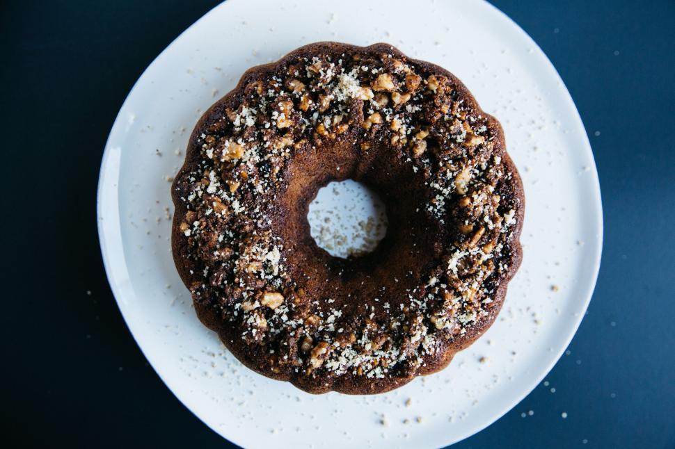 Free Image of Nut-topped bundt cake on white plate with dark background. 