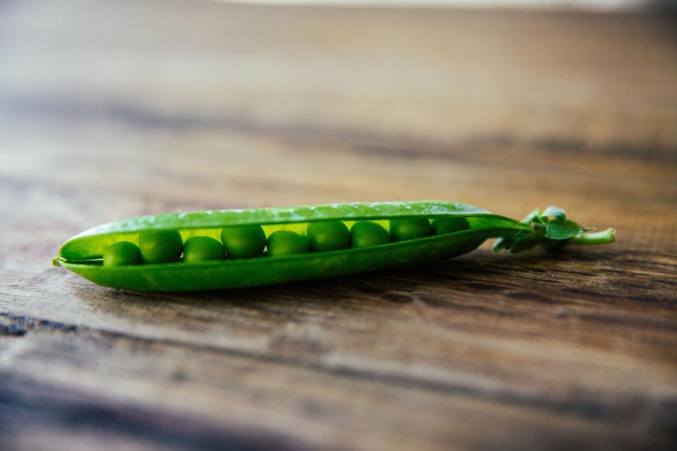 Free Image of Single pea pod with green peas lined up on a wooden table. 