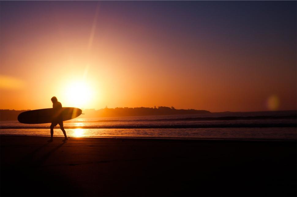 Free Image of Surfer walking with surfboard at sunset on a beach. 