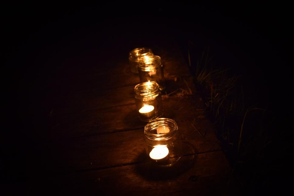 Free Image of Four glowing candles in jars on a dark wooden path 