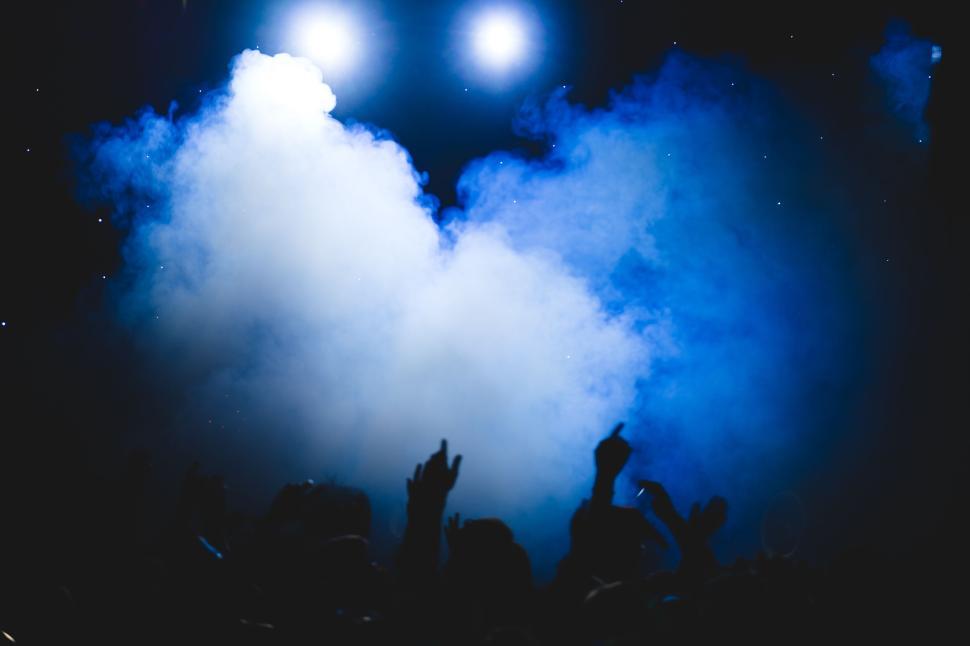 Free Image of Concert crowd with hands raised under smoky blue lights. 