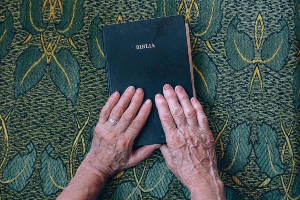 Free Image of Old hands holding a bible on detailed patterned cloth. 