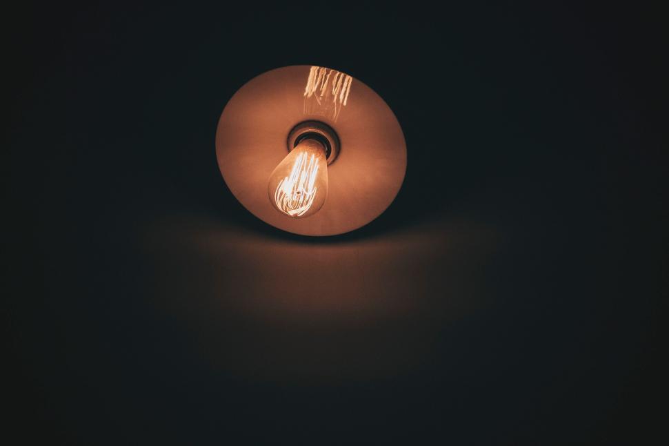 Free Image of Single light bulb glowing in a dark minimalist room. 