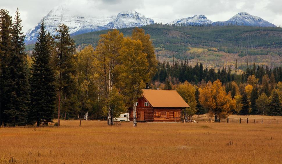 Free Image of Log cabin in autumn meadow with mountains in background. 