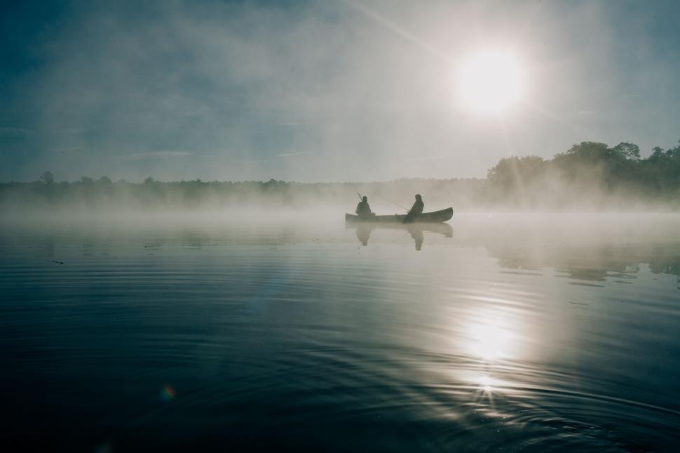Free Image of Two people canoeing on a misty lake at sunrise. 