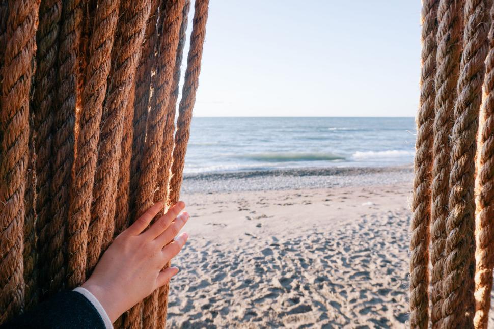 Free Image of Hand pushing aside rope curtain to reveal a sandy beach. 