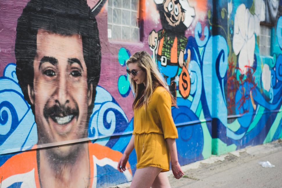 Free Image of Woman in yellow walking past graffiti on colorful wall 