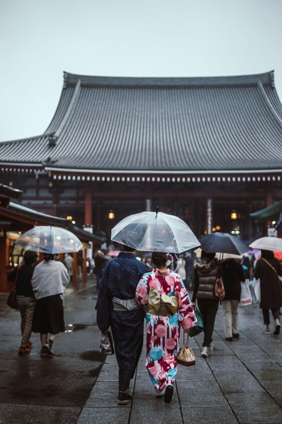 Free Image of People with umbrellas walking near traditional temple 