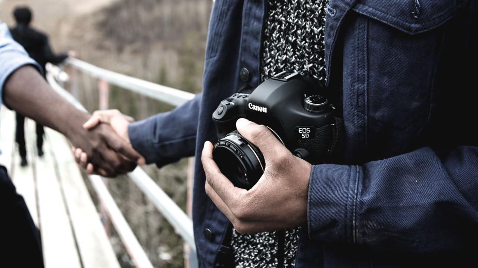 Free Image of Person holding a Canon camera while shaking hands outdoors. 