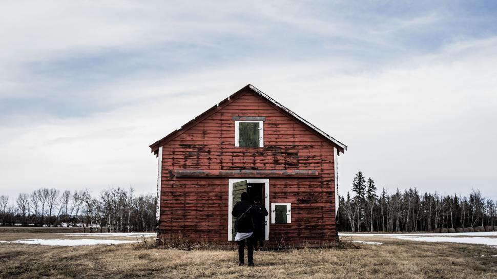 Free Image of Person entering a weathered red barn with grassy meadow. 