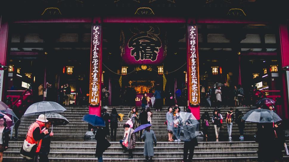 Free Image of People with umbrellas walking towards a large shrine 