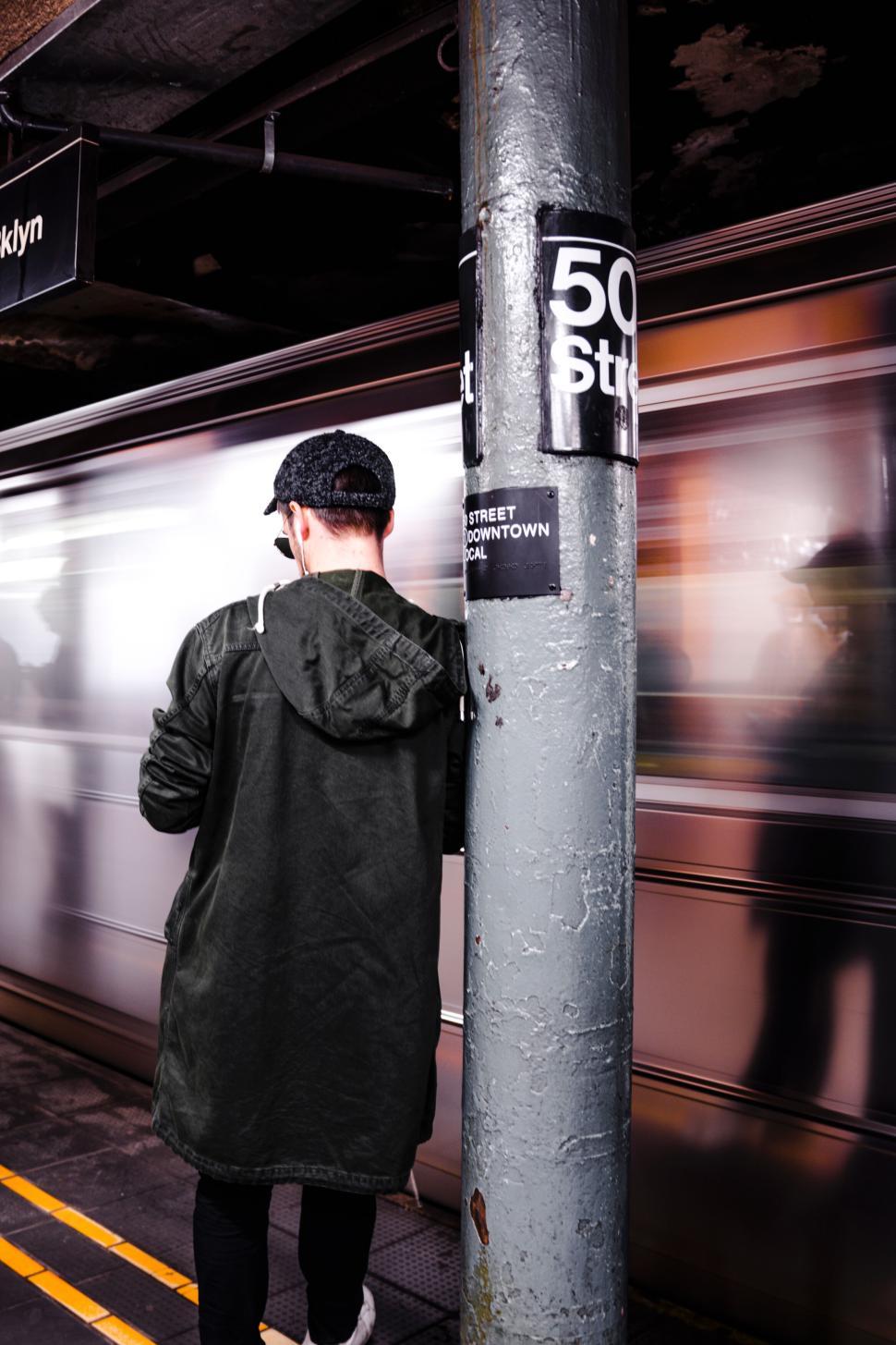 Free Image of Man leaning on a pole in subway station with train motion 