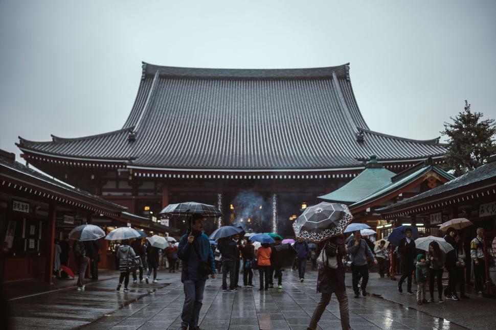 Free Image of Tourists with umbrellas at a traditional temple in rain. 
