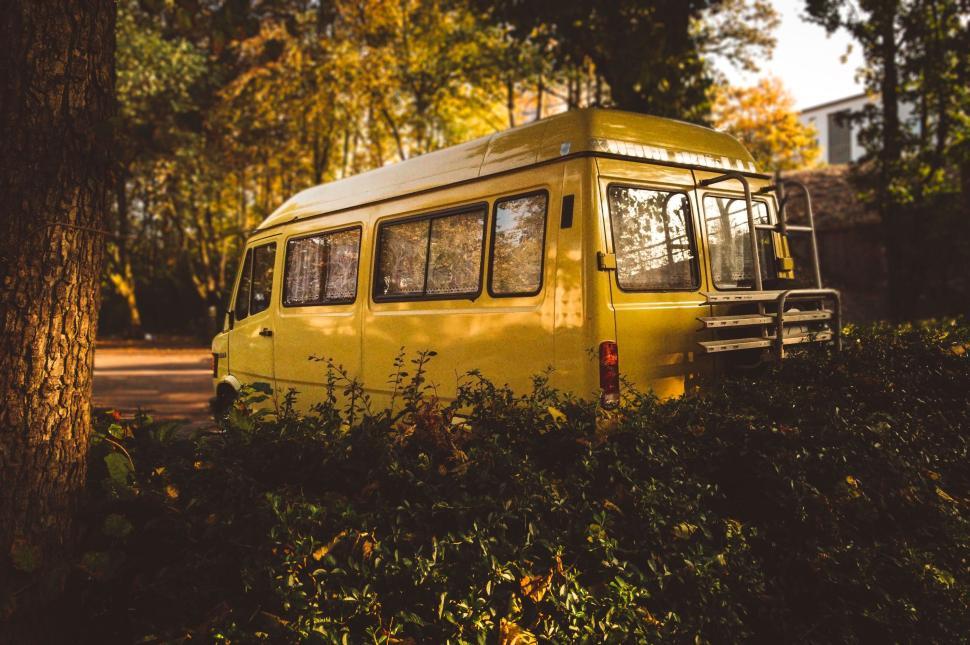 Free Image of Bright yellow van parked in a scenic autumn forest setting 