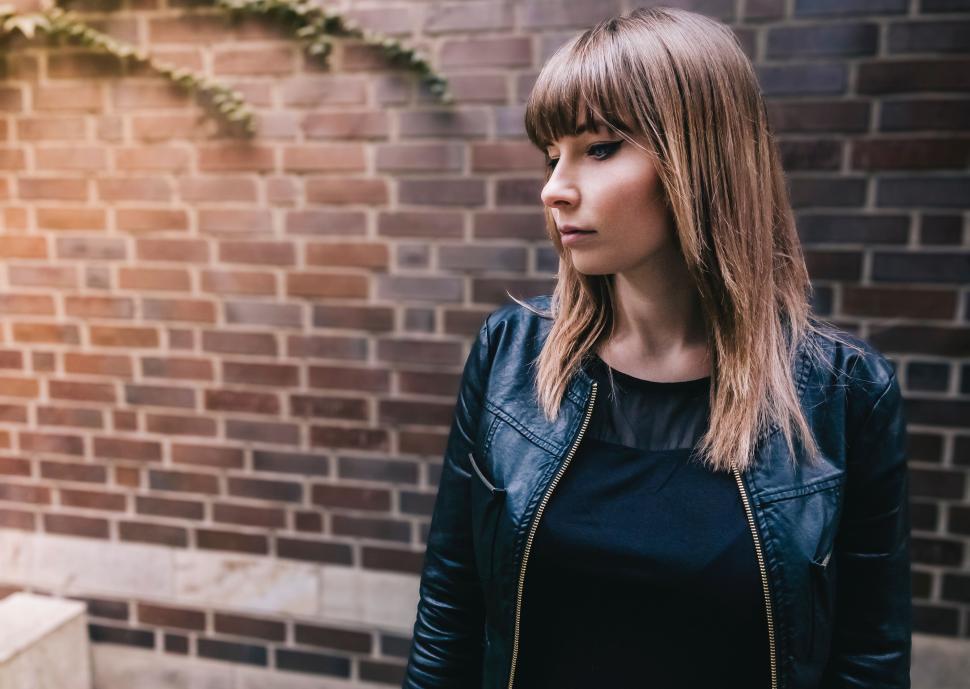 Free Image of Woman in black jacket with brick wall background 