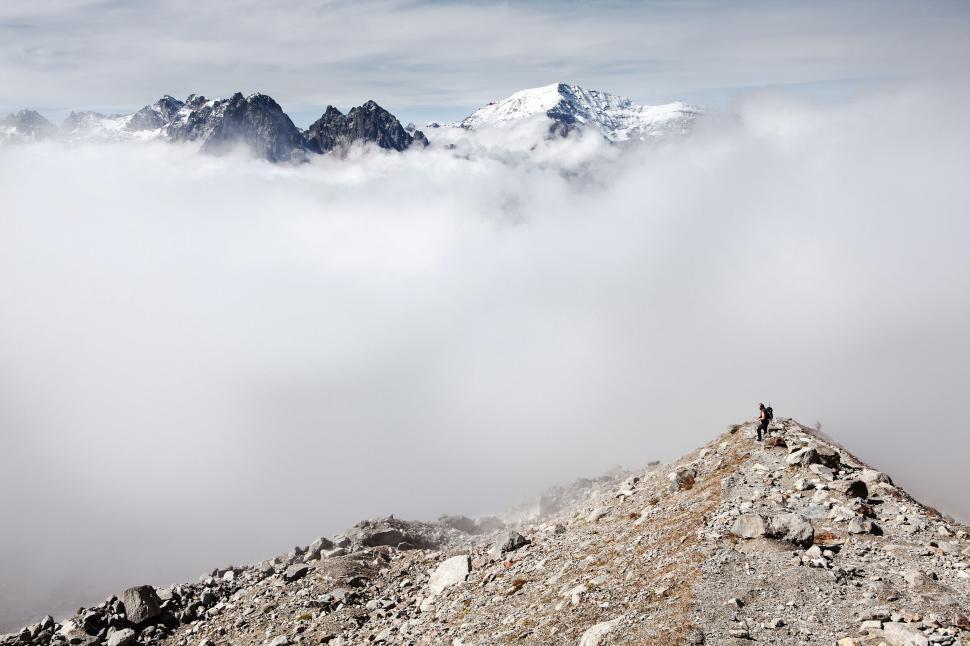 Free Image of Person hiking on rocky trail above a cloud blanket. 