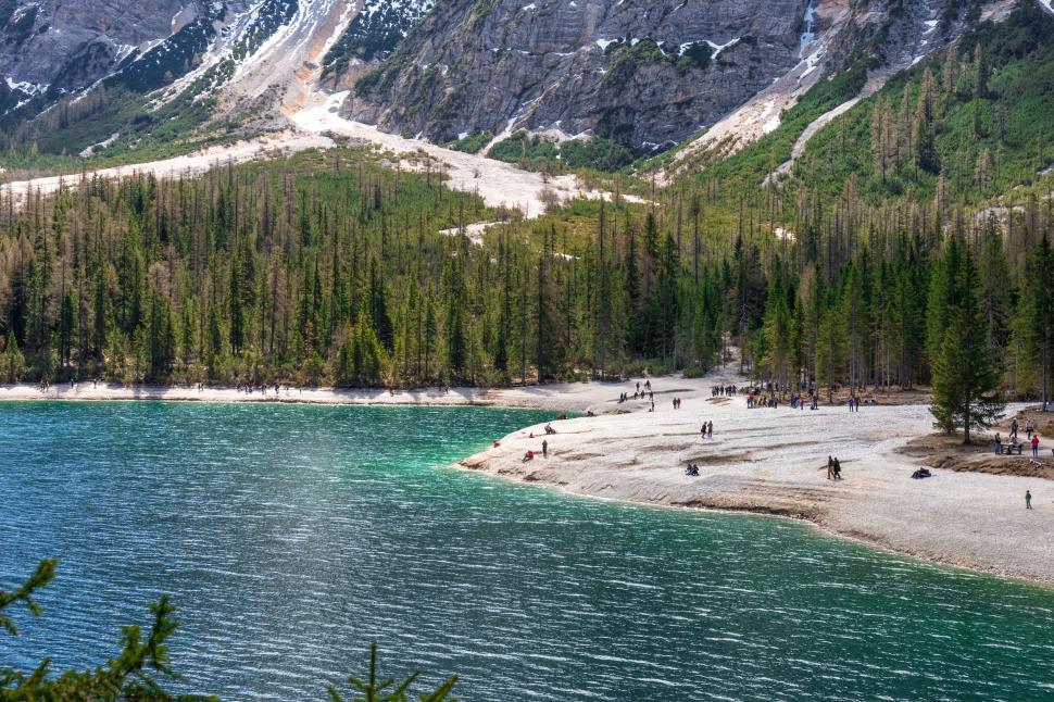 Free Image of Lakeside view with mountains, trees, and people relaxing. 