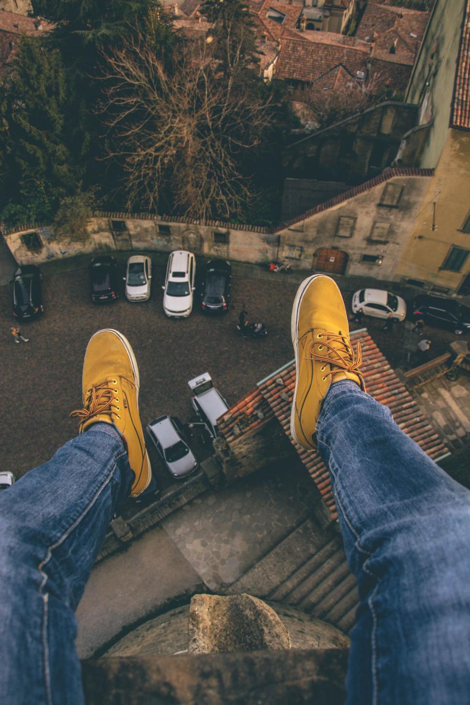 Free Image of Feet in yellow shoes dangling from a high building 