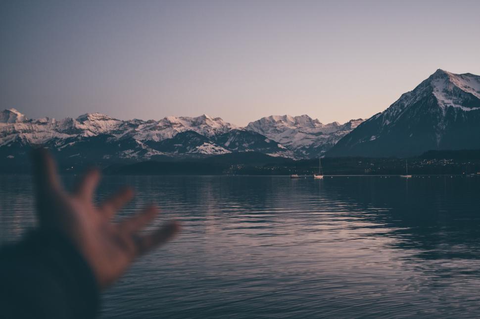 Free Image of Hand reaching out to serene mountain lake at dusk 