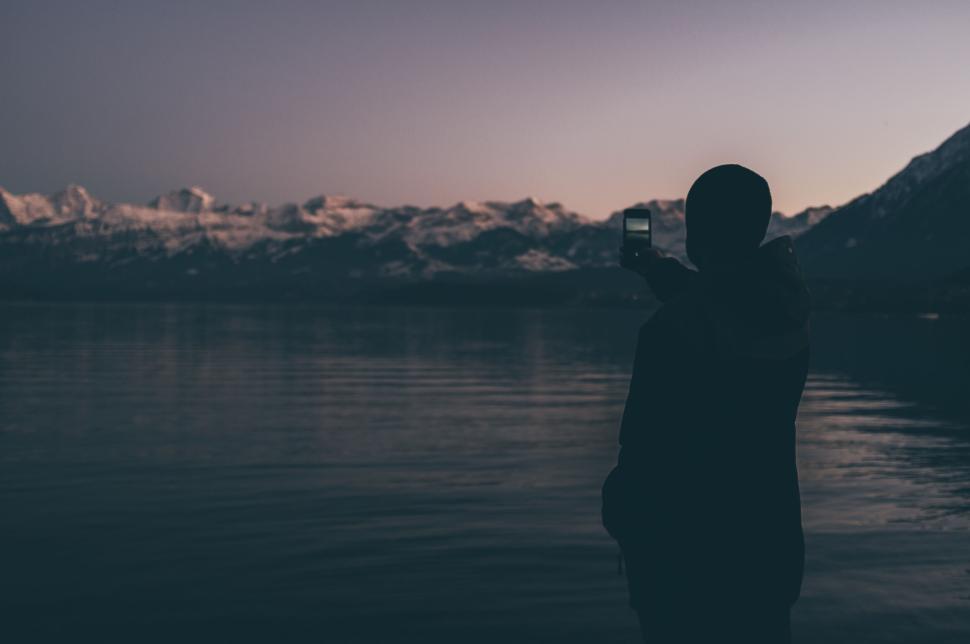 Free Image of Silhouette taking a photo of serene lake and mountains 