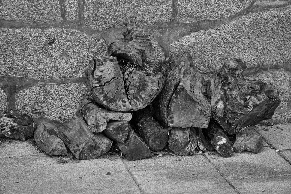 Free Image of Pile of cut wood stacked against a stone wall. 