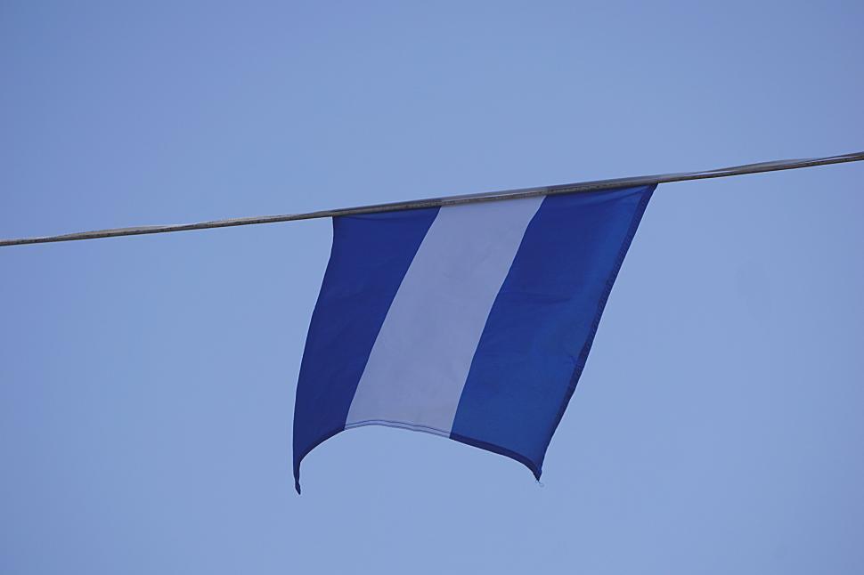 Free Image of Blue and white flag hanging on a wire against the sky. 