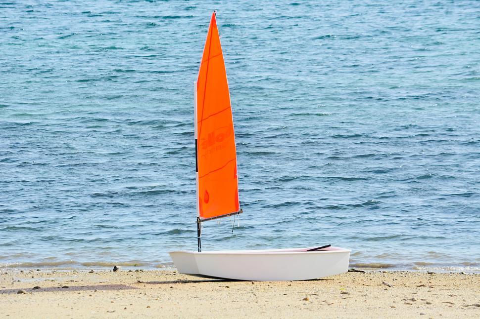 Free Image of Orange sailboat on sandy beach with clear blue water. 