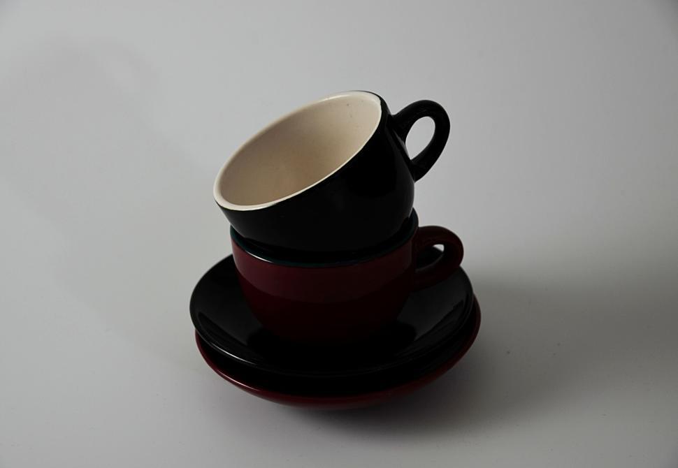 Free Image of Stacked black and red cups with saucers on white backdrop. 