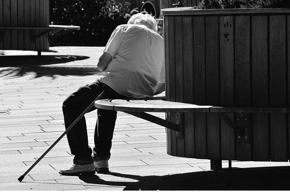 Free Image of An elderly man with a cane sitting alone on a bench 