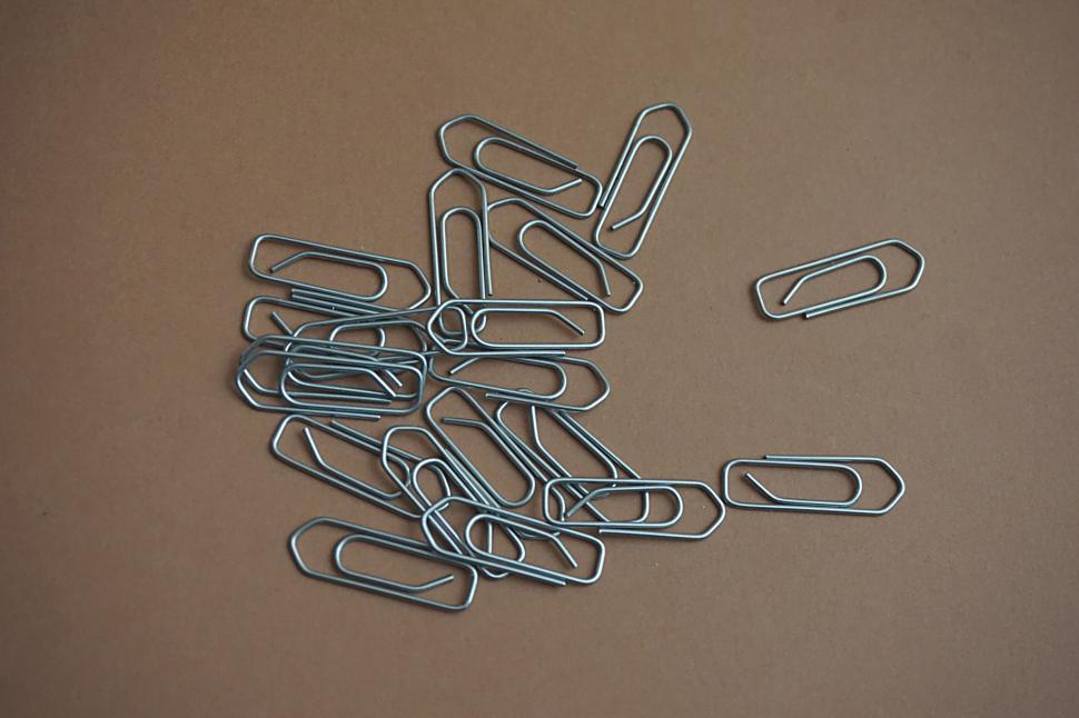 Free Image of Pile of metallic paper clips scattered on brown paper. 