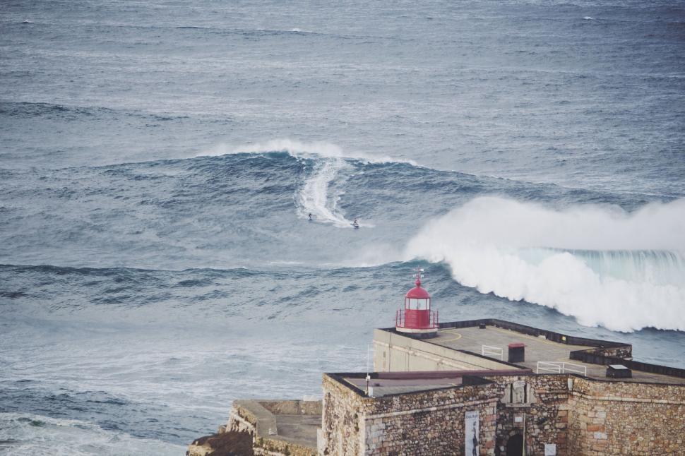 Free Image of Surfer catching large wave near lighthouse on shore 