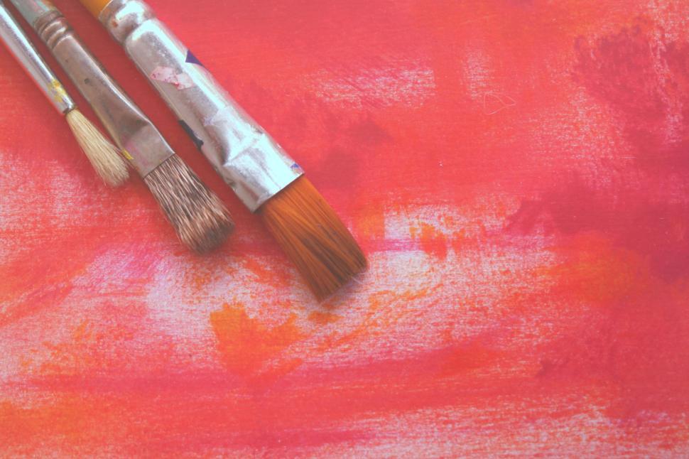 Free Image of Three used paintbrushes on a textured red canvas background. 