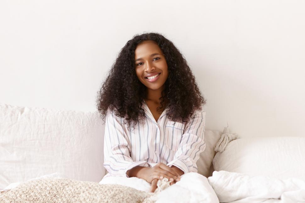 Free Image of Cute joyful young African female in stylish pajamas relaxing in bed, smiling broadly at camera. Beautiful dark skinned girl with Afro hairstyle spending slow lazy morning at home, having happy look 