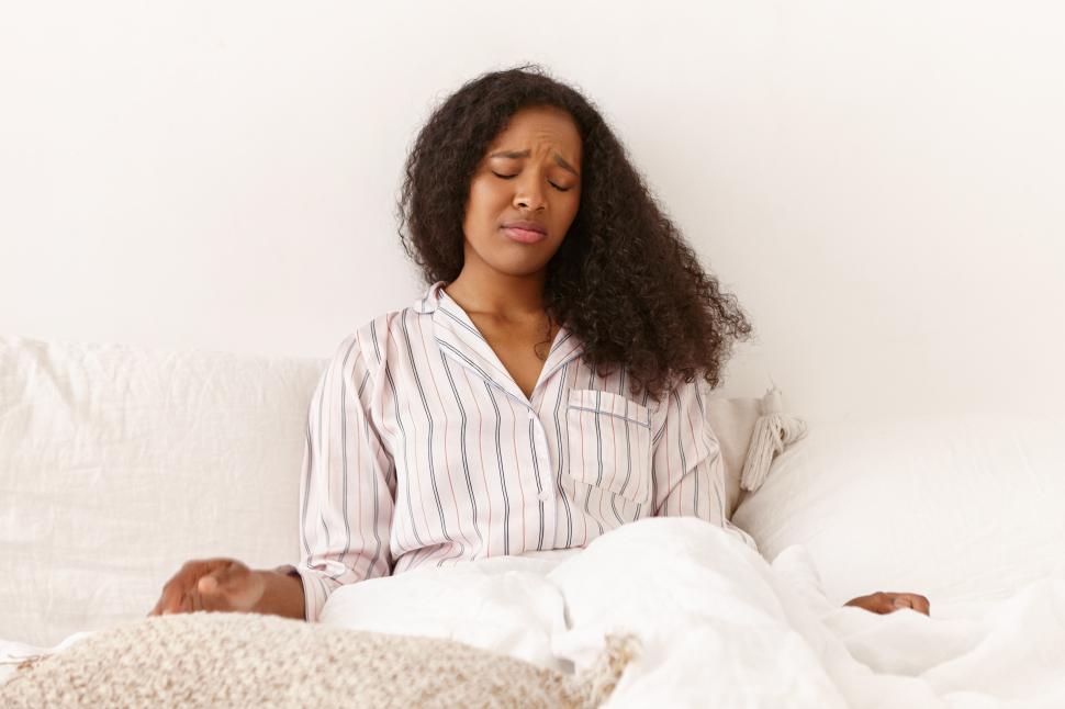 Free Image of Indoor shot of upset young dark skinned female with messy voluminous hair sitting in bed having frustrated mournful facial expression because she slept over, being late for work. Stress and depression 