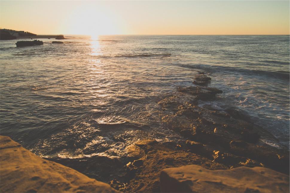 Free Image of Sunset over ocean with rocky coastline in view 