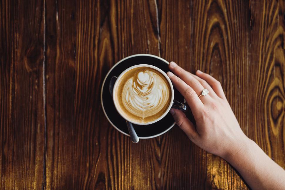 Free Image of Hand holding a cup of coffee with latte art on a table. 