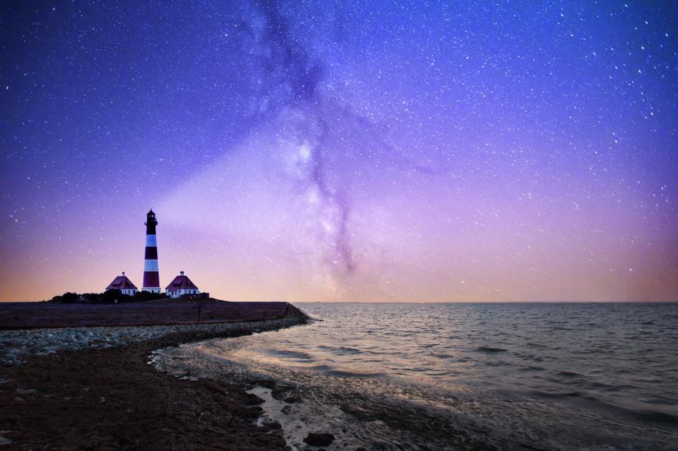Free Image of Lighthouse under a starry sky by the ocean at night. 