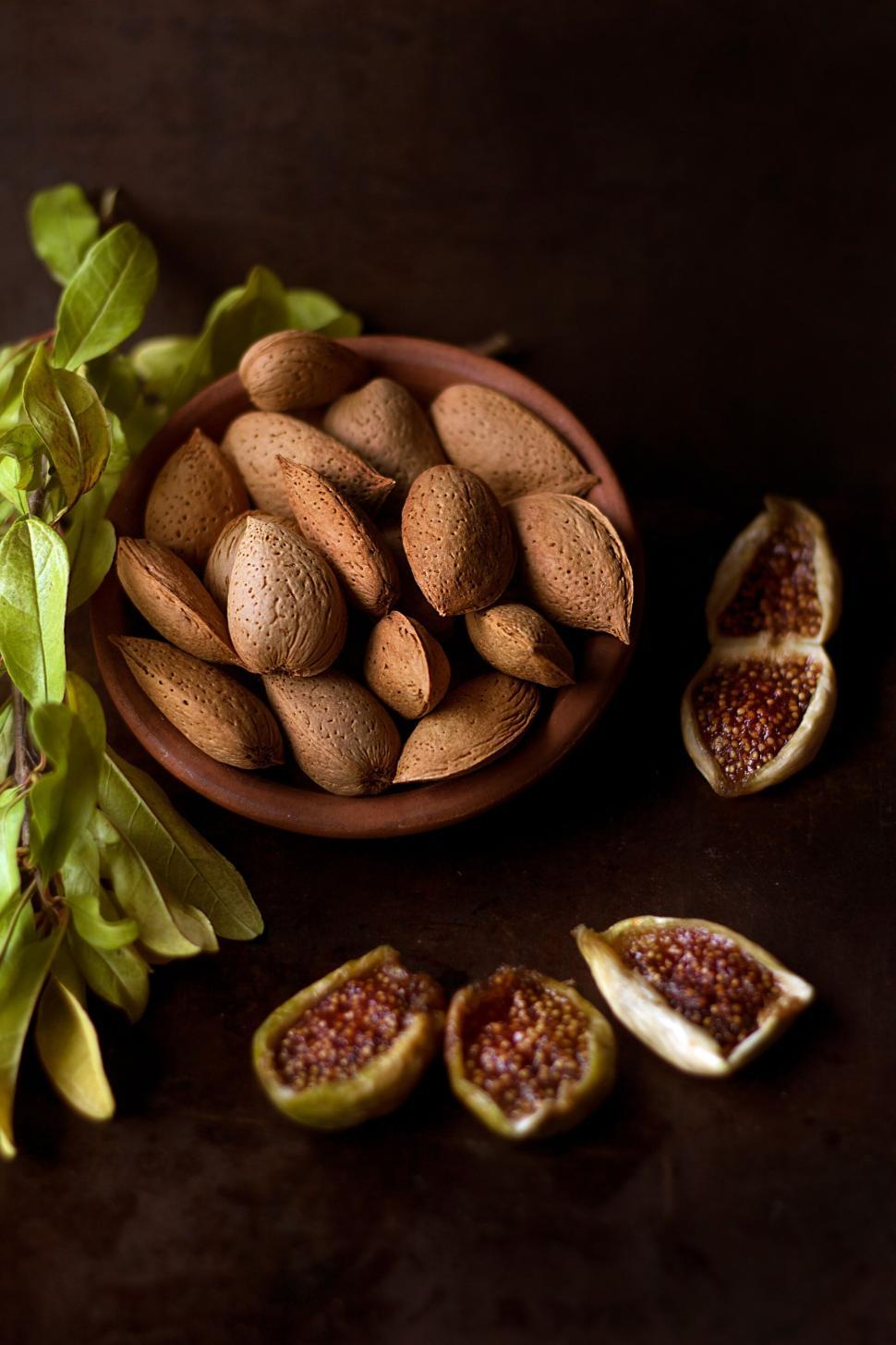 Free Image of Dish of almonds and figs with green leaves on display 